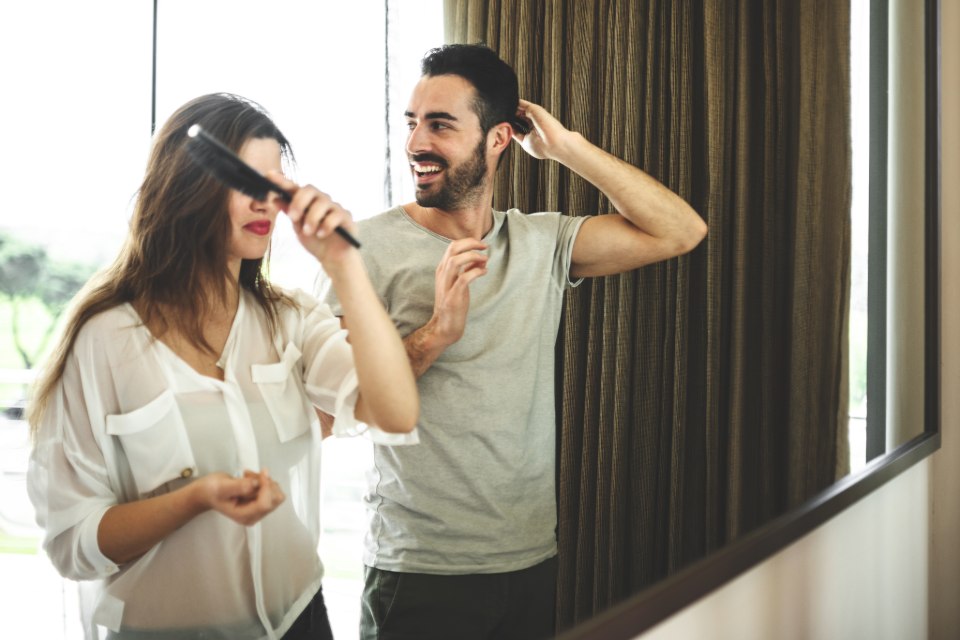 A couple, man and woman, standing in front of a mirror, each combing their hair.