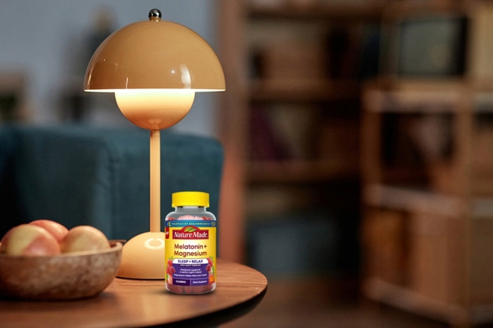 Magnesium 300 mg + Ashwagandha 125 mg Capsules on a night stand next to a lamp.