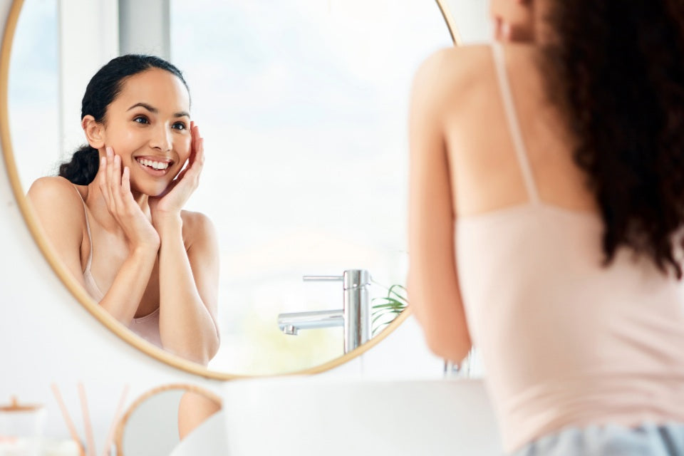 Person examining their skin in a bathroom mirror as part of a daily skincare routine.