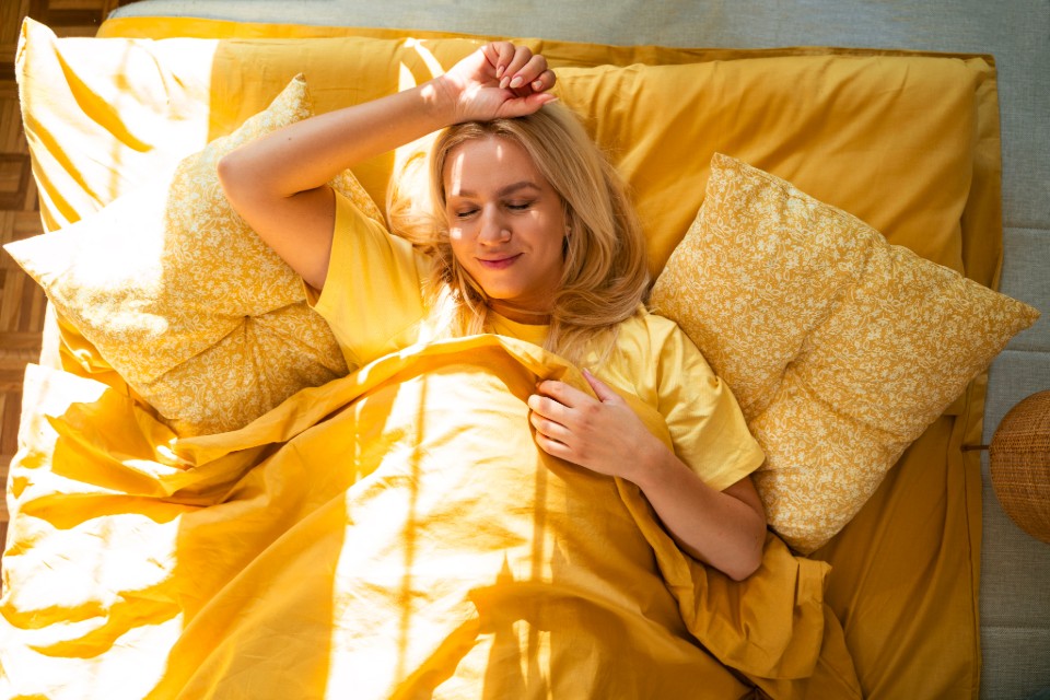 Person lying in bed under yellow bedding with sunlight.