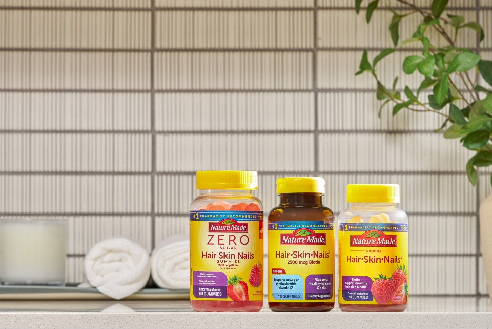 Nature Made Hair, skin, and nails supplement bottles displayed on a bathroom counter with towels and greenery.