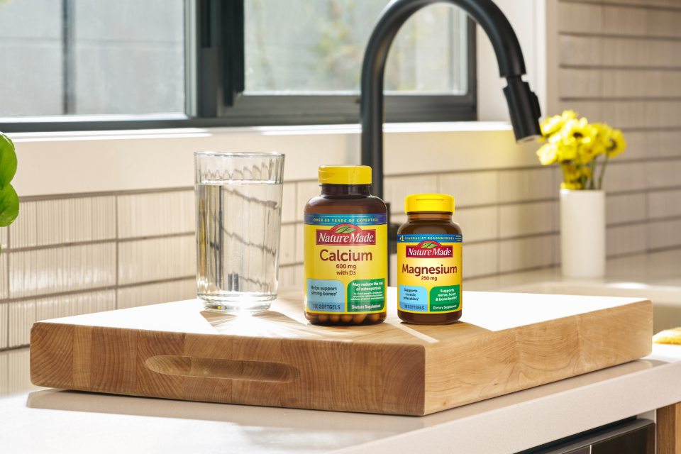 Nature Made Calcium 600mg & Magnesium 250mg bottles on a chopping board next to a glass of water.