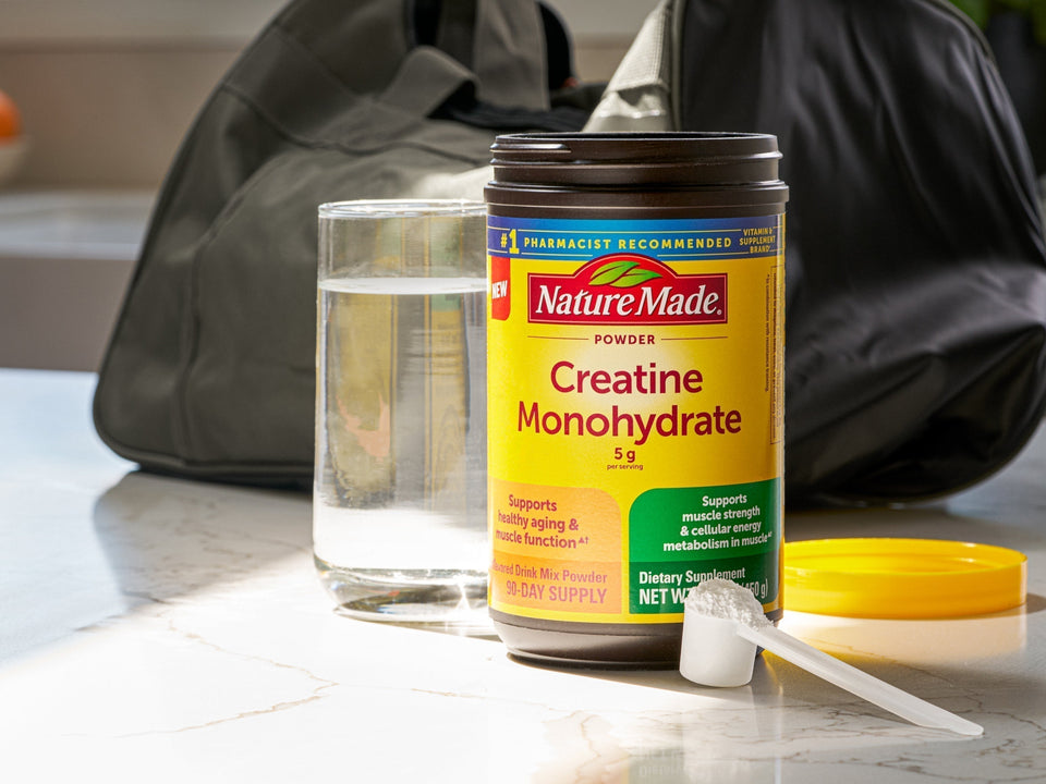 Nature Made Creatine Monohydrate, a glass of water, gym bag and scoop of creatine on a countertop.