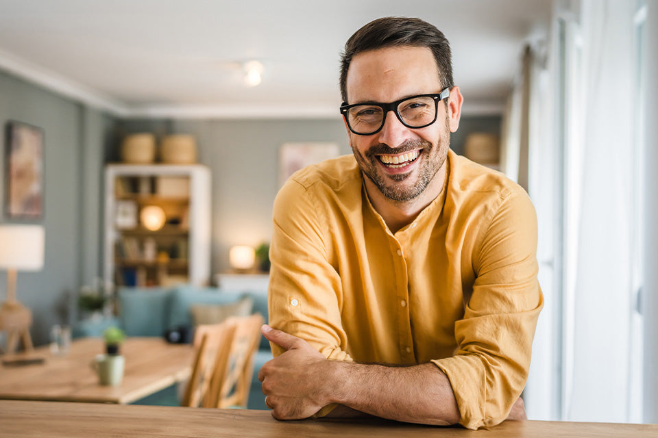 Man in a yellow sweater with arms crossed in a living room setting.