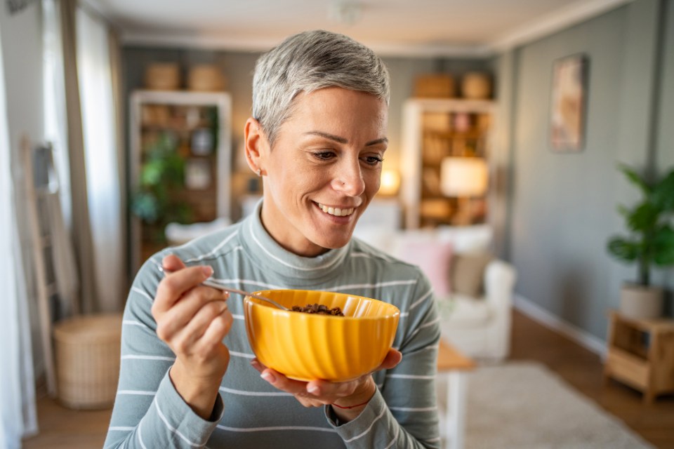 Person in grey striped shirt standing in a living room and eating out of a yellow bowl.