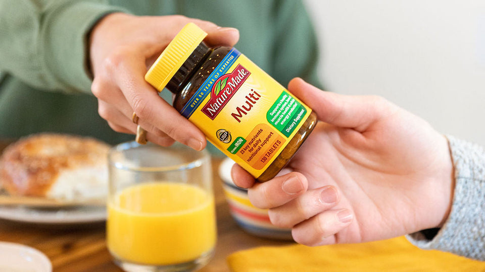 Nature Made Multi multivitamin bottle being handed over at a breakfast table with orange juice