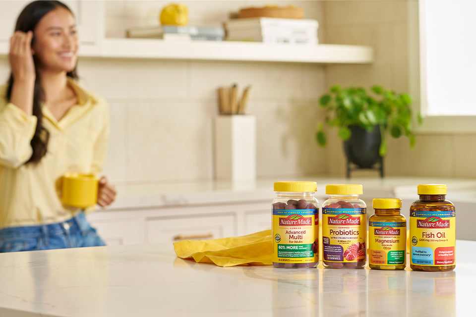 Nature Made vitamins and supplements on a kitchen counter with yellow napkin, featuring Advanced Multi, Probiotics, Magnesium, and Fish Oil bottles.