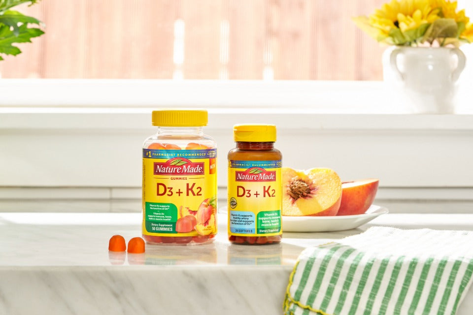 Nature Made Vitamin D3 + K2 bottles and gummies on a kitchen counter top next to sliced peaches.