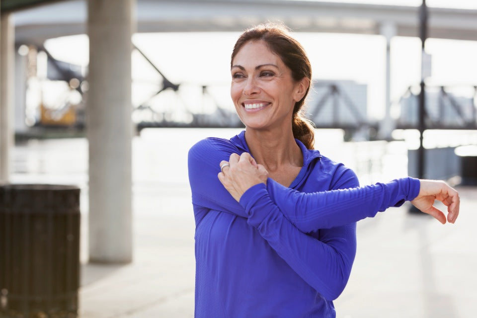 Woman in a purple fleece workout top, stretching her arm.