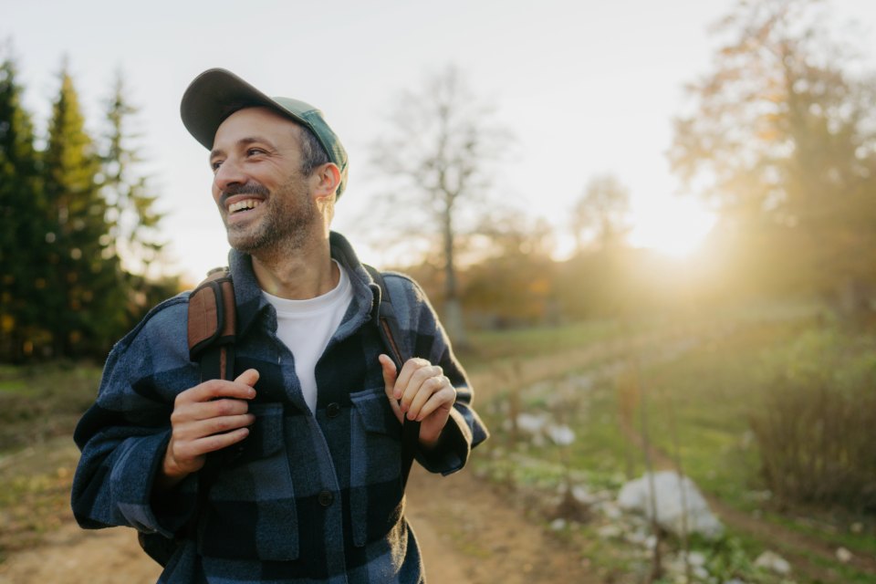 Person in a blue plaid shirt in the outdoors with trees and a hiking trail in the background.