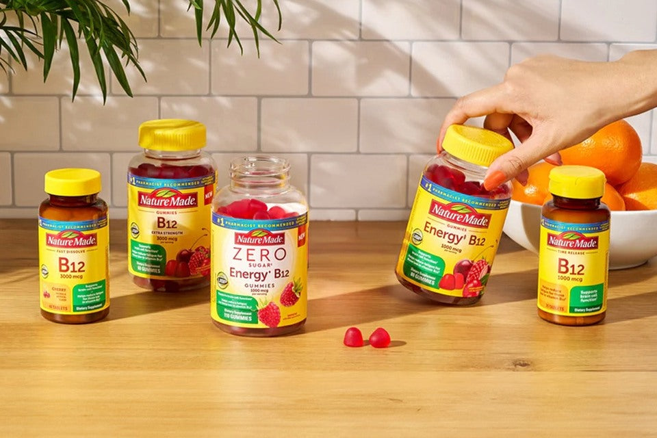 Nature Made B vitamin bottles on a wooden surface with a hand picking up one of them.