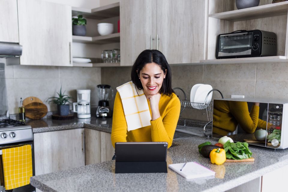 Person in yellow sweater sitting in a well lit kitchen on a tablet device.
