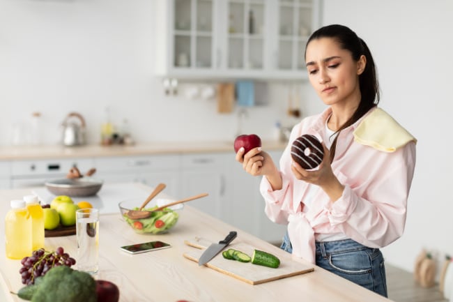 A woman comparing a nutritious apple to a sugary donut