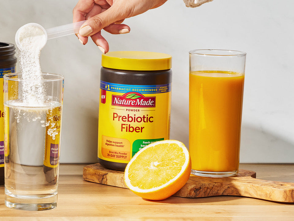 Nature Made Prebiotic Fiber on counter with a glass of water and a glass of orange juice.