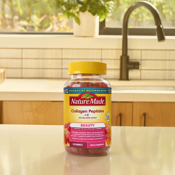 A bottle of Nature Made Collagen Peptides + C dietary supplement with a yellow cap, standing on a kitchen counter with a sink and window in the background.