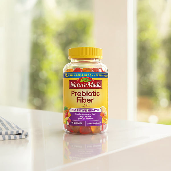 A bottle of Nature Made Prebiotic Fiber Gummies sits on a white countertop with a blurred kitchen background. 