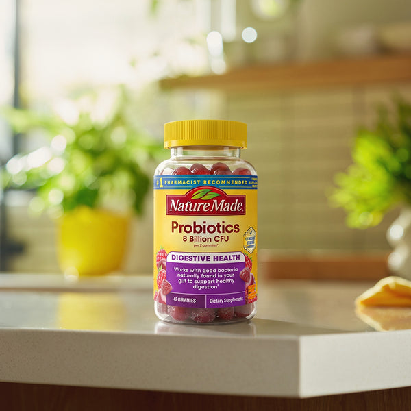 A bottle of Nature Made Probiotics dietary supplement with a yellow cap and yellow label, standing on a kitchen counter with a blurred warm-toned interior background.