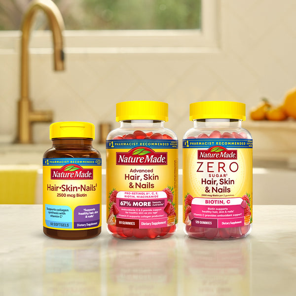 Three Nature Made supplement bottles on a kitchen counter: Hair, Skin, and Nails; Advanced Hair, Skin, and Nails; and Zero Sugar Hair, Skin, and Nails, with a blurred kitchen background.