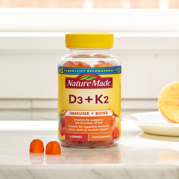 A bottle of Nature Made D3 + K2 gummies on a marble countertop with a blurred kitchen background and two loose gummies in front.