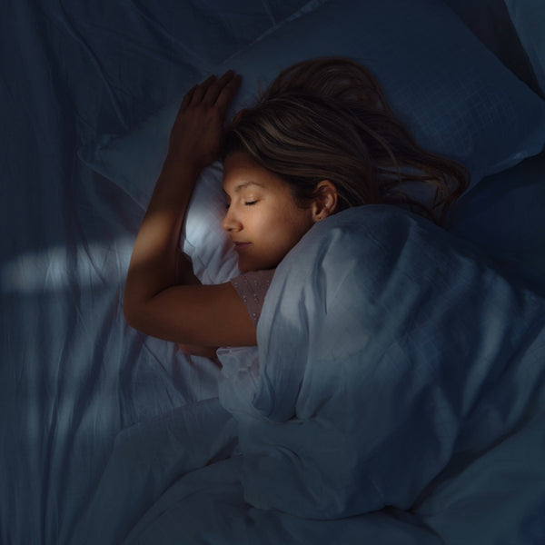 A woman sleeping soundly in bed, wrapped in a cool blue blanket under soft window light.